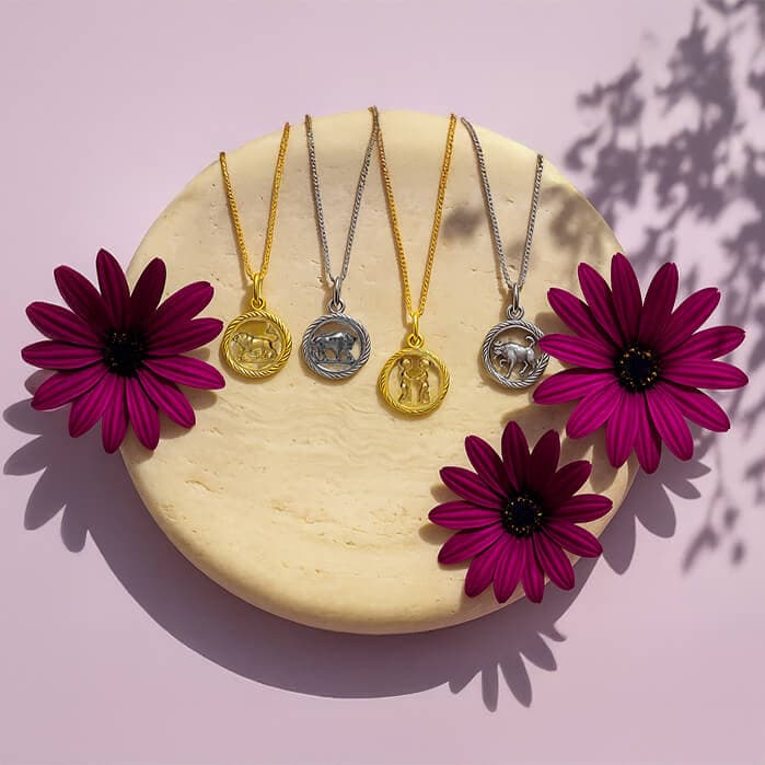 Stjerne tegn-smykker (anheng) i gull og sølv utstilt på en beige sirkulær flate med to livlige lilla blomster på en rosa bakgrunn.