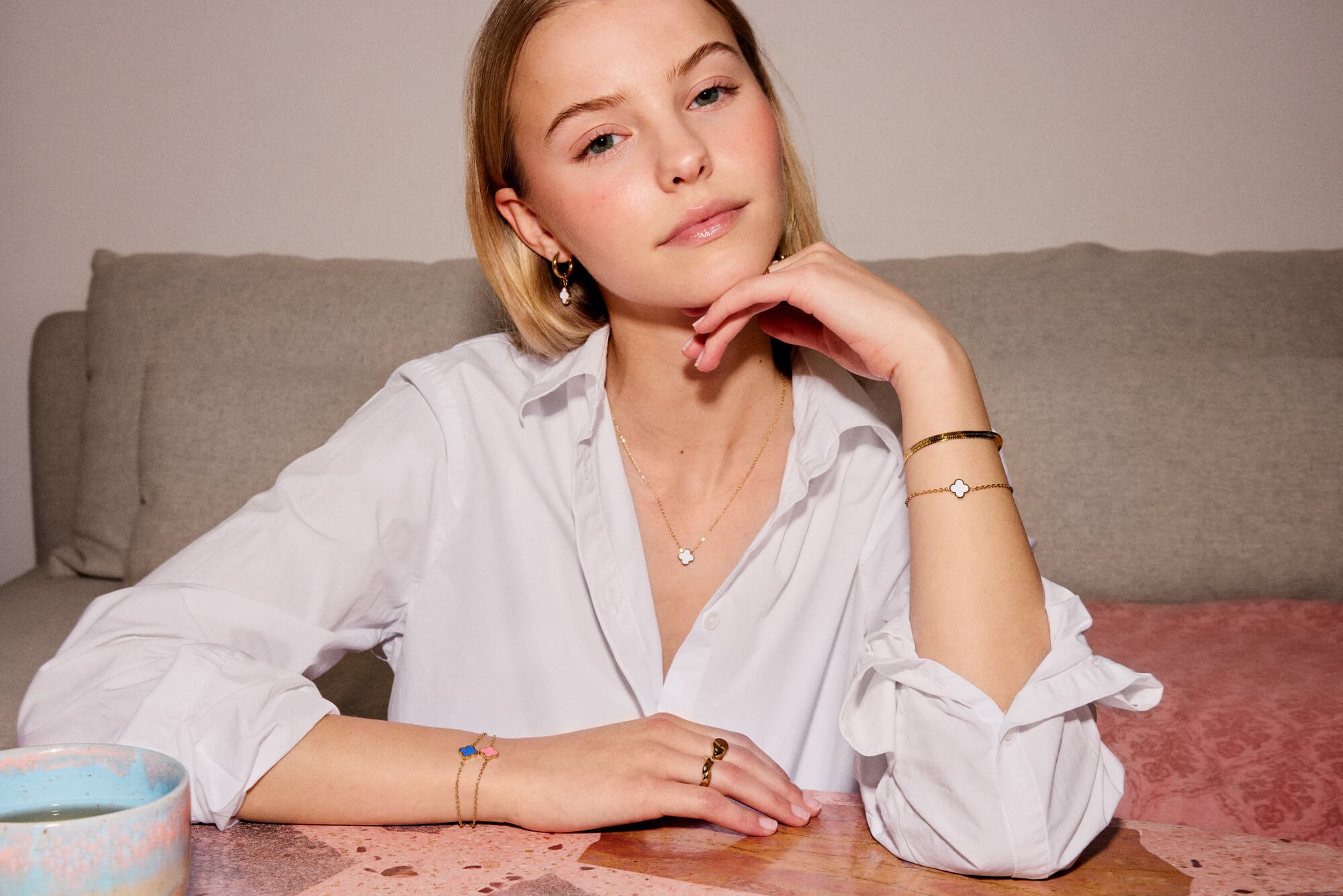 ByOlea of Norway Modellen fra by Olea smiler bredt i sort skinnjakke foran en bokhylle, mens hun setter håret sitt opp i en hestehale.