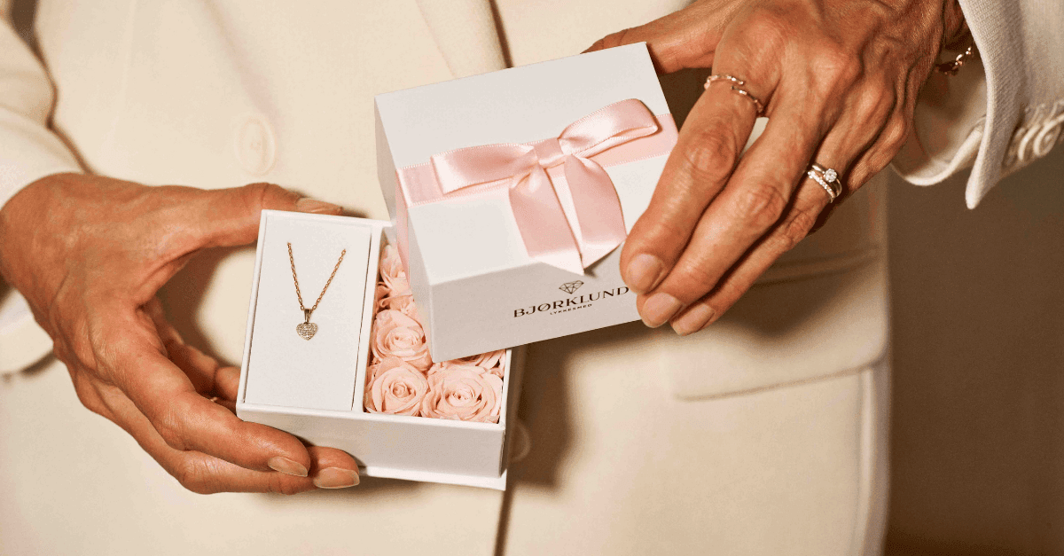 Julegave fra henne En kvinne med rosa kjole holder en hvit gaveeske med rosa bånd på utsiden og rosa roser på innsiden