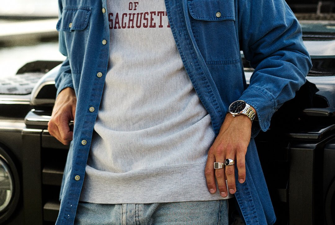 Bjørklund har flotte ringer til herre Mann iført olajakke og lys genser viser hånd med sølvringer og armbåndsur foran sort bil.