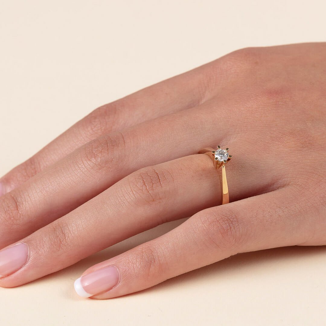 Et nærbilde av en godt vedlikehold kvinnehånd med diamantring. Dette er en gullring med seks klør som holder en liten diamant på plass.