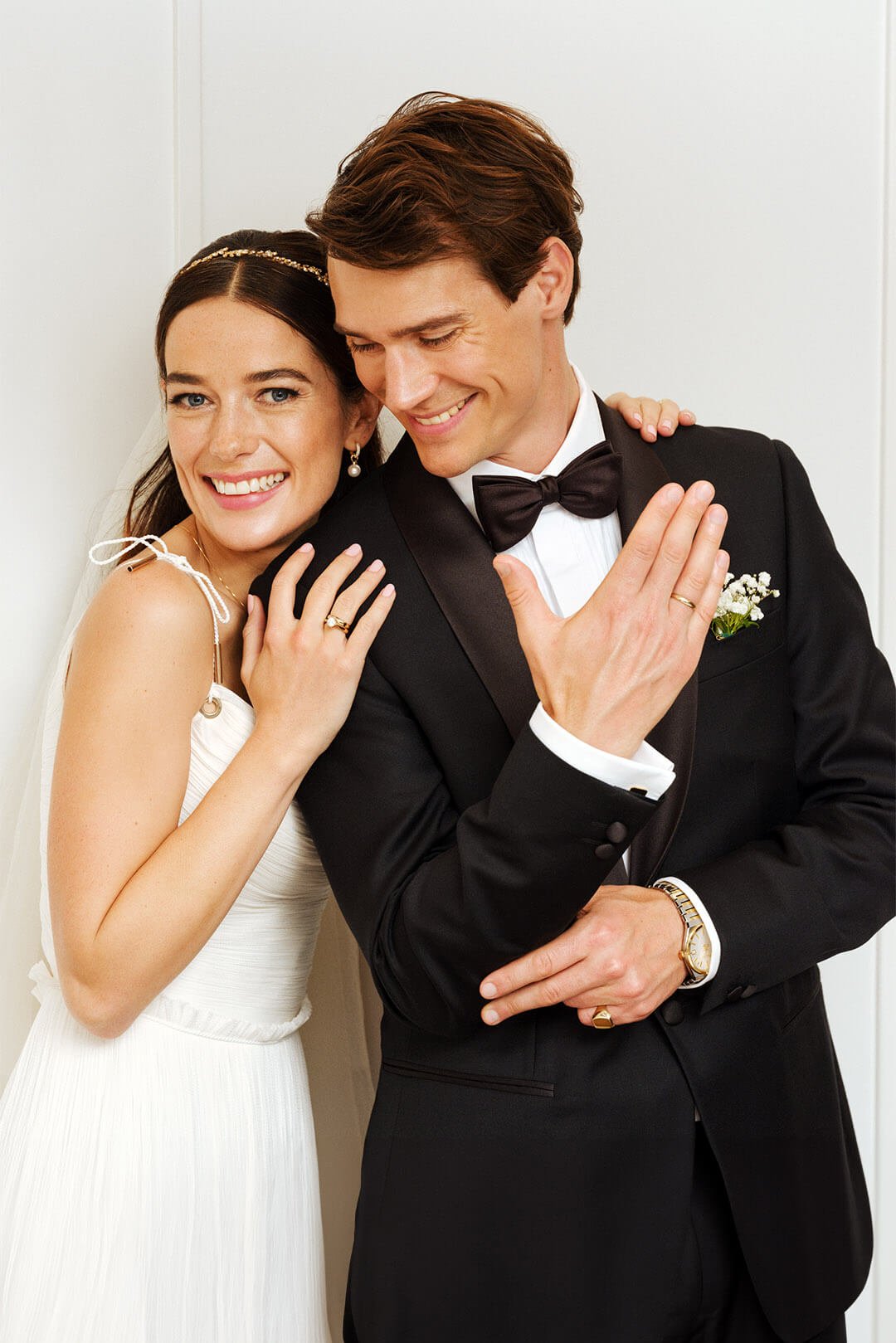 En nygift par i Tuxedo og bryllupskjole smiler mens de klemmer hverandre og viser frem ringene sine. Les mer om gifteringer fra Duette