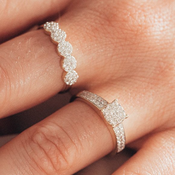 Diamantringer Nærbilde av fingre med to ringer der små hvite diamanter pryder hele ringen rundt, der ene har en større diamant i midten.