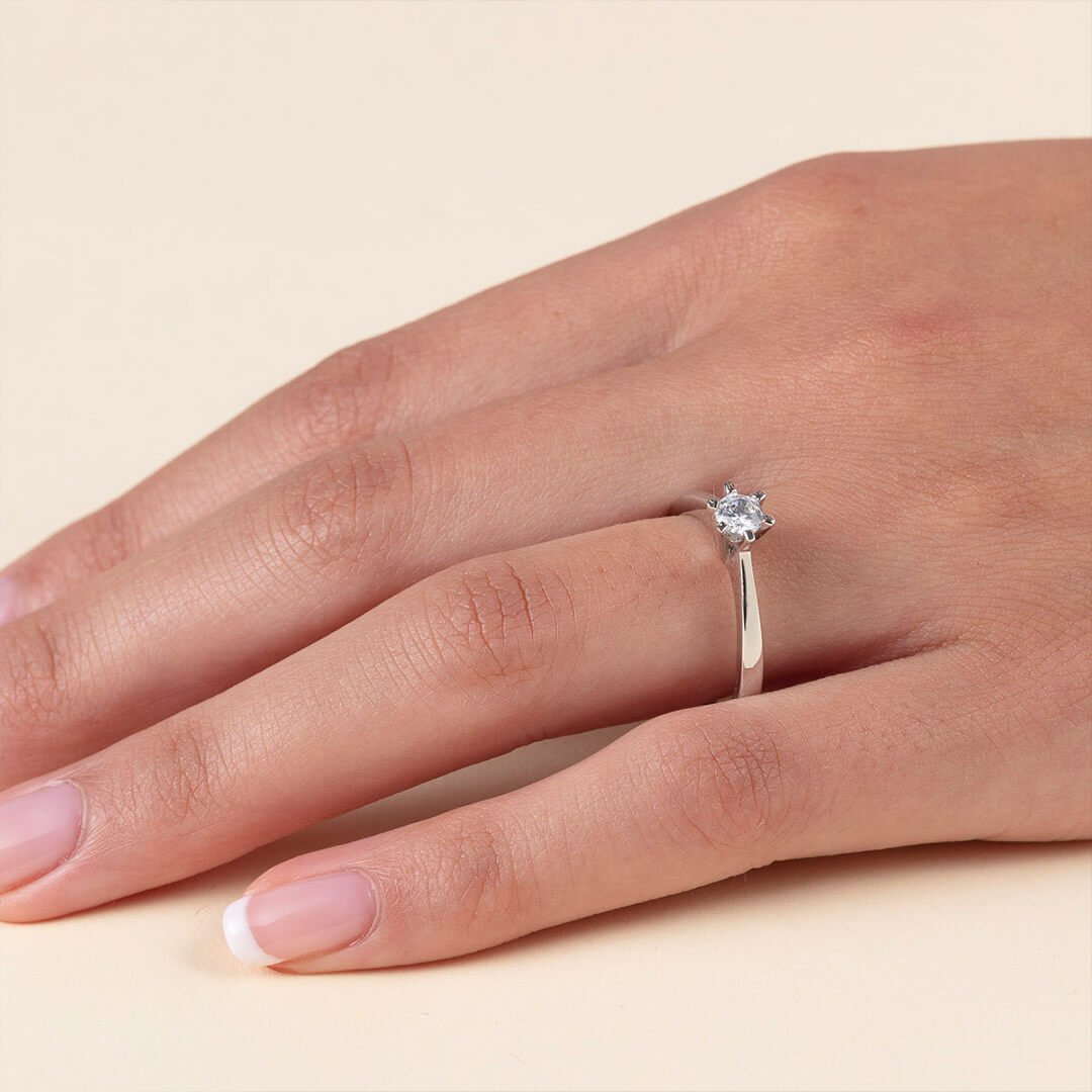 Diamantring i hvitt gull En velbevart venstre kvinnehånd som ligger på beige overflate og bakgrunn, for å stille ut diamantringen hun har på fingeren.