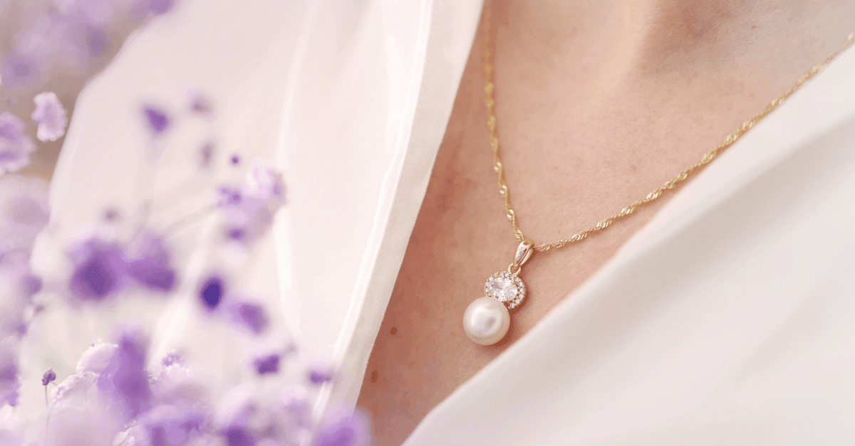 Se våre perleøredobber Nærbilde av en kvinne med halssmykke og perleanheng. Kvinnen har hvit bluse og holde lille blomster